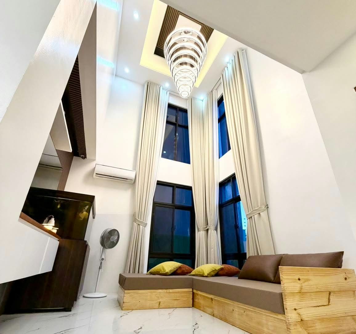 Double-height living area with a wood-framed sofa and tall windows
