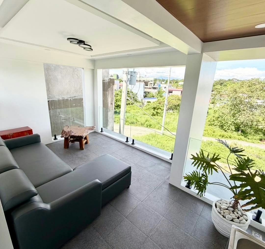 Covered balcony seating with glass railings and a view of greenery